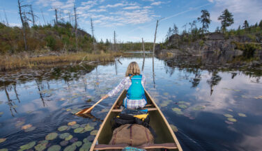 A woman in a canoe paddles among rocks and lilypads in the Boundary Waters.